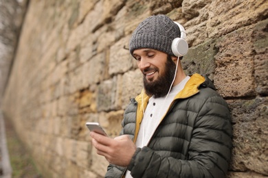 Photo of Mature man with headphones listening to music near stone wall. Space for text