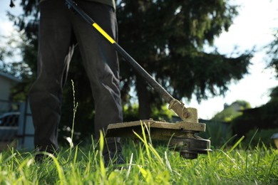 Photo of Man cutting green grass with string trimmer outdoors, closeup