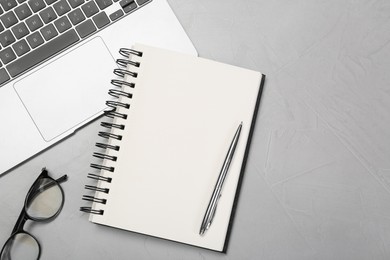 Photo of Open notebook, laptop, pen and glasses on light grey table, flat lay