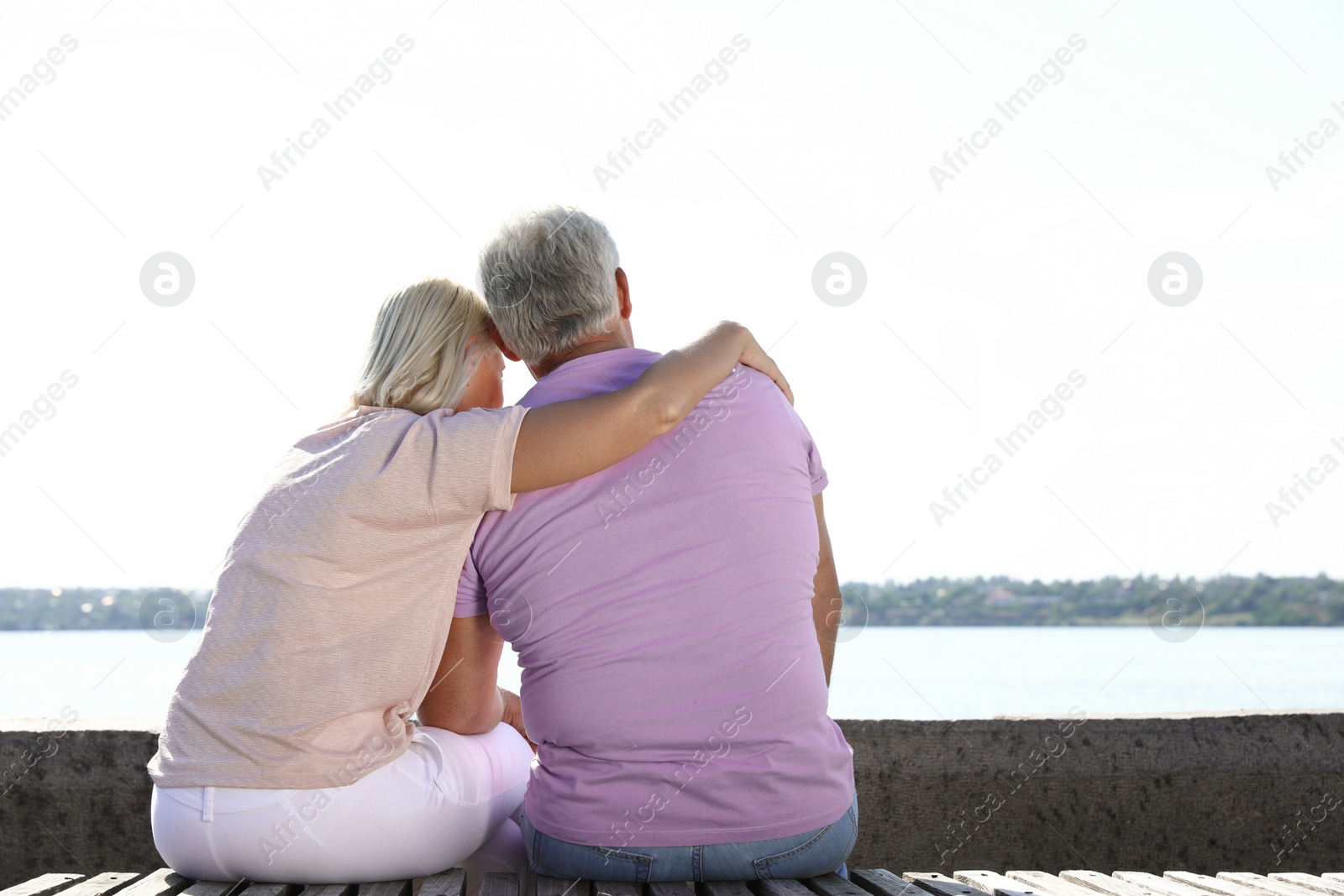 Photo of Affectionate senior couple sitting near river together on sunny day. Space for text