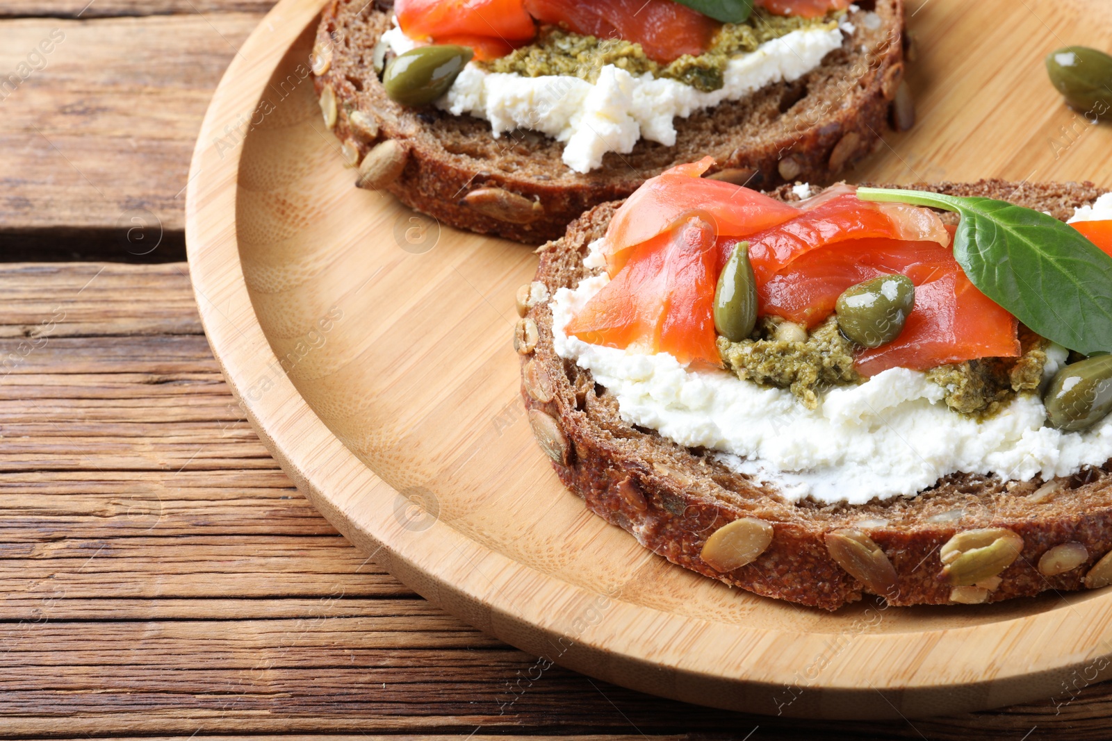 Photo of Delicious sandwiches with cream cheese, salmon, capers and pesto on wooden table, closeup
