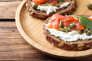 Delicious sandwiches with cream cheese, salmon, capers and pesto on wooden table, closeup