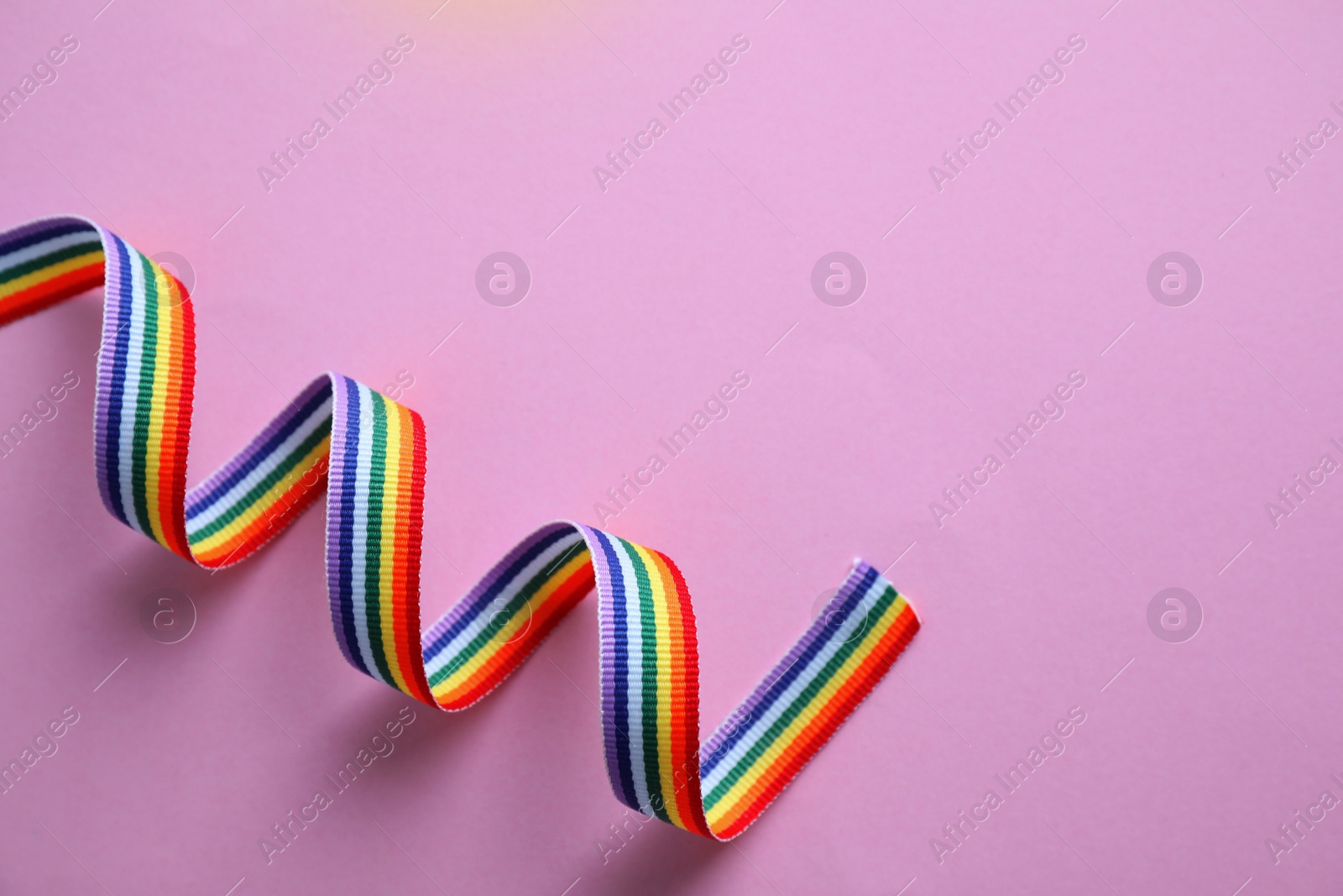 Photo of Bright rainbow ribbon on color background, top view with space for text. Symbol of gay community