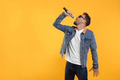 Handsome man with sunglasses and microphone singing on yellow background. Space for text