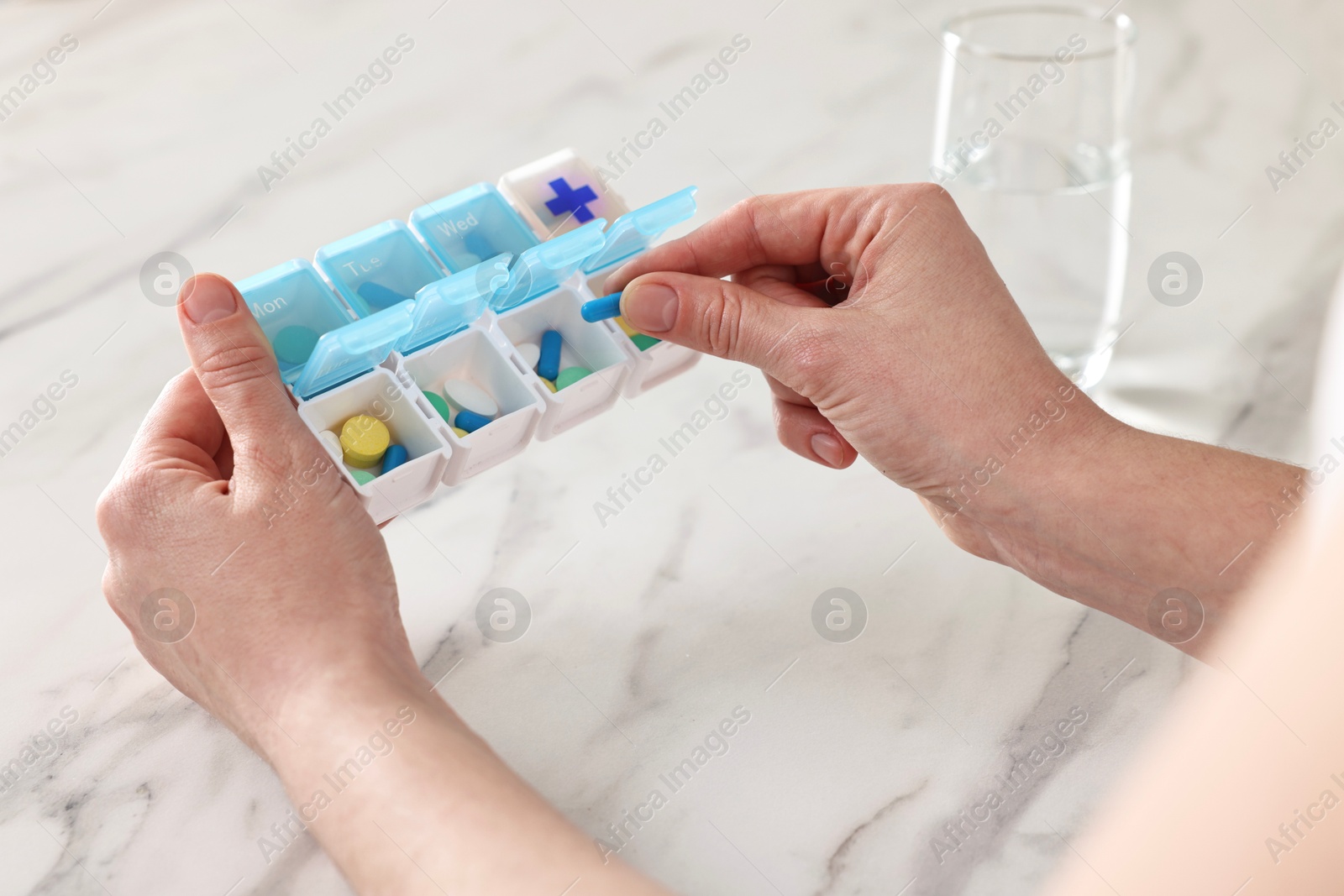 Photo of Woman with pills, organizer and glass of water at white marble table, closeup