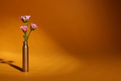 Photo of Bullet cartridge case and beautiful chrysanthemum flowers on orange background, space for text