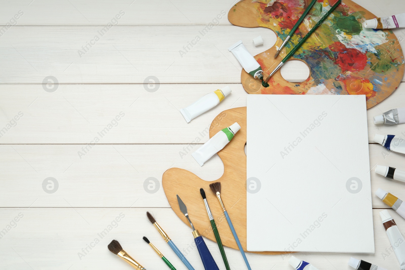 Photo of Blank canvas, brushes, palettes and paints on white wooden table, flat lay. Space for text