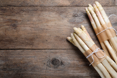 Photo of Bunches of fresh white asparagus on wooden table, flat lay. Space for text