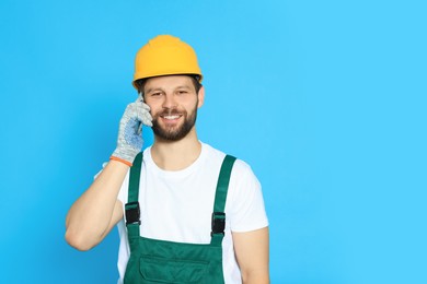 Professional repairman in uniform talking on smartphone against light blue background. Space for text