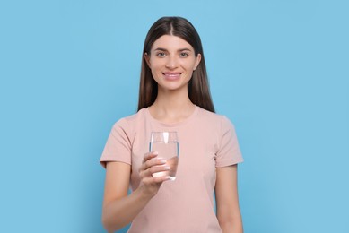 Healthy habit. Portrait of woman holding glass with fresh water on light blue background