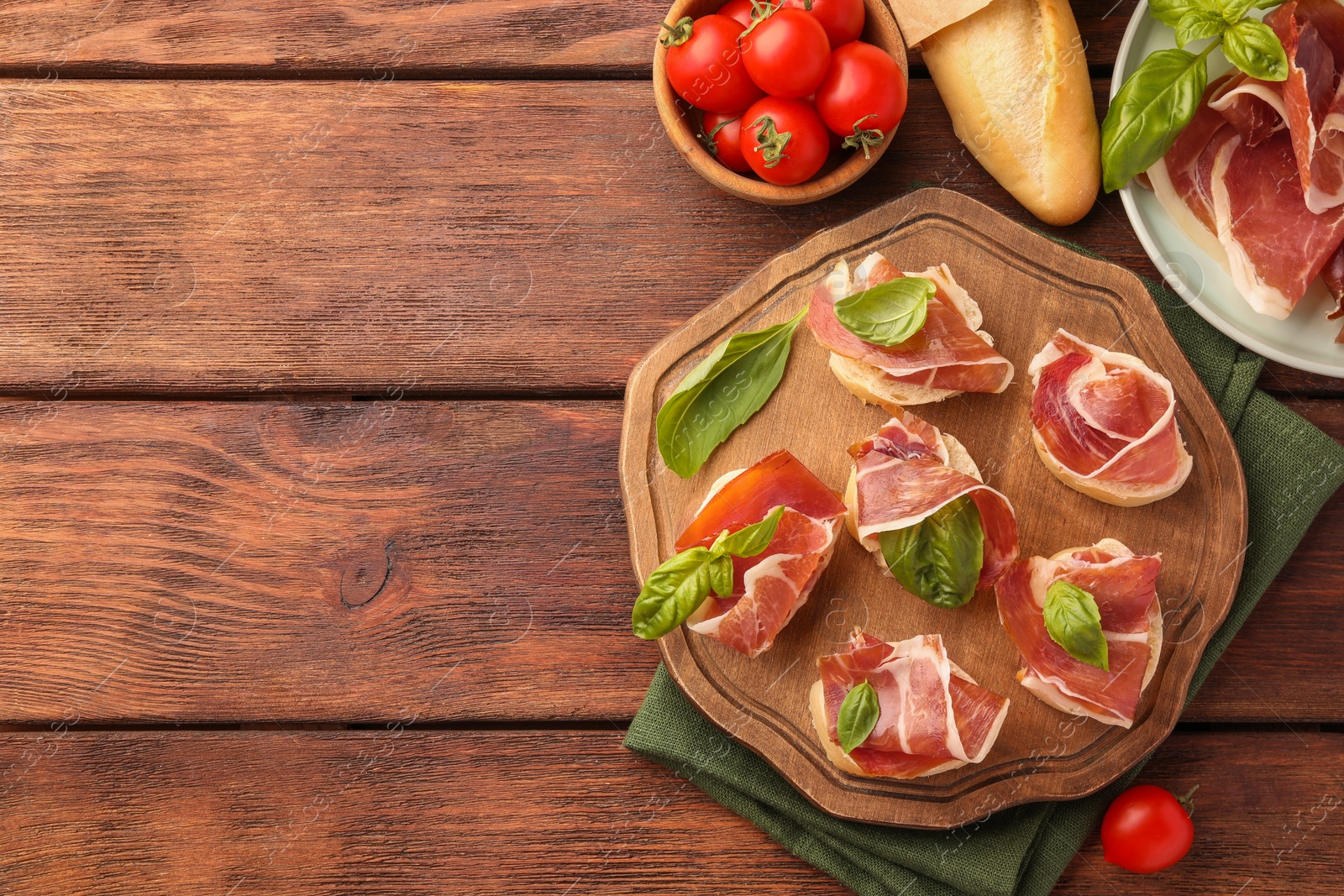 Photo of Tasty sandwiches with cured ham, basil leaves and tomatoes on wooden table, flat lay. Space for text