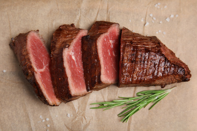 Photo of Delicious sliced beef tenderloin with rosemary on parchment, flat lay