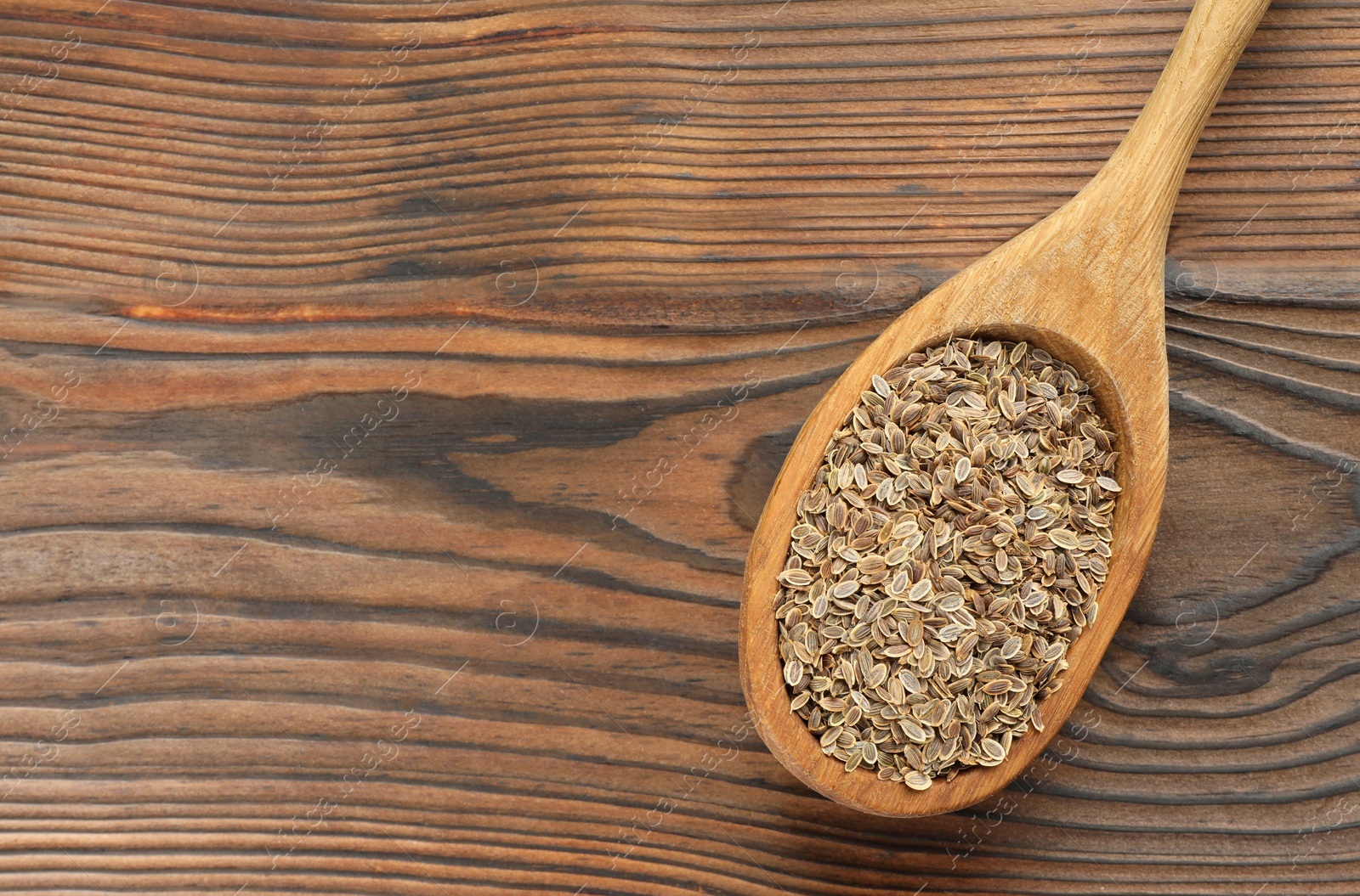 Photo of Spoon of dry dill seeds on wooden table, top view. Space for text