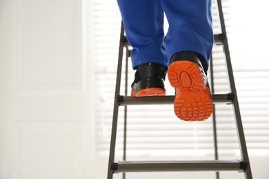Professional worker climbing up ladder indoors, closeup view