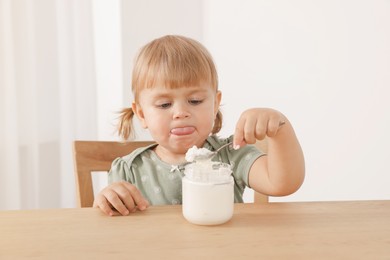 Photo of Cute little child eating tasty yogurt with spoon at wooden table indoors