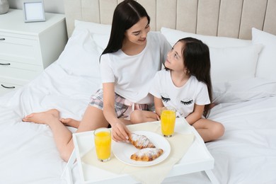 Photo of Young mother and her daughter having breakfast on bed at home