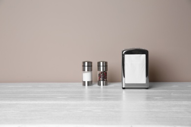 Photo of Napkin holder with salt and pepper shakers on table against color background. Space for text