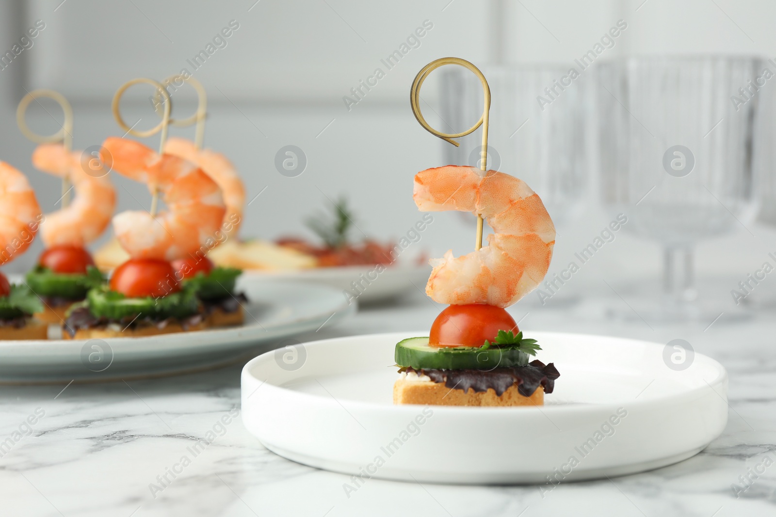 Photo of Tasty canapes with shrimps, cucumber, greens and tomatoes on white marble table