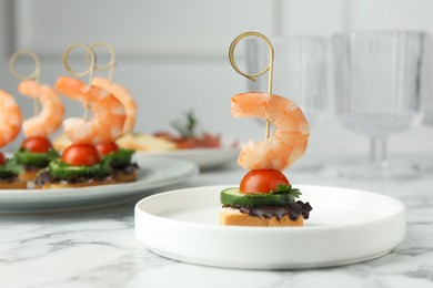 Photo of Tasty canapes with shrimps, cucumber, greens and tomatoes on white marble table