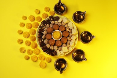 Photo of Happy Diwali. Flat lay composition with diya lamps, chrysanthemum flowers and delicious Indian sweets on yellow table