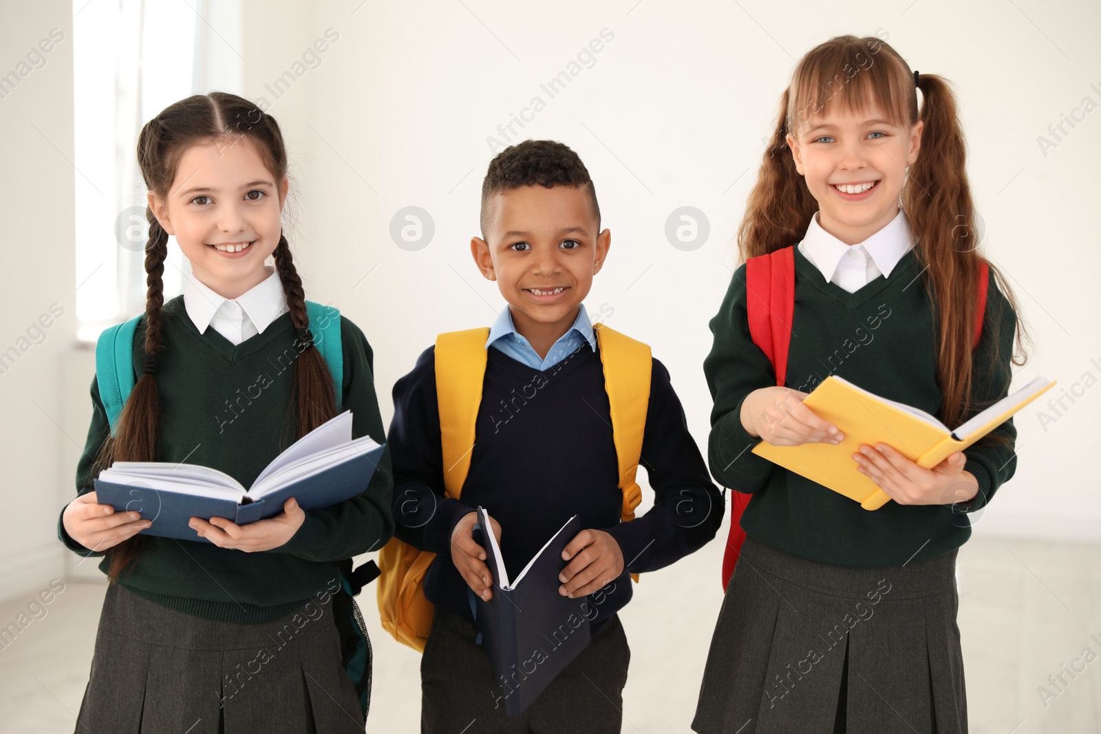 Photo of Portrait of cute children in school uniform with backpacks and books indoors