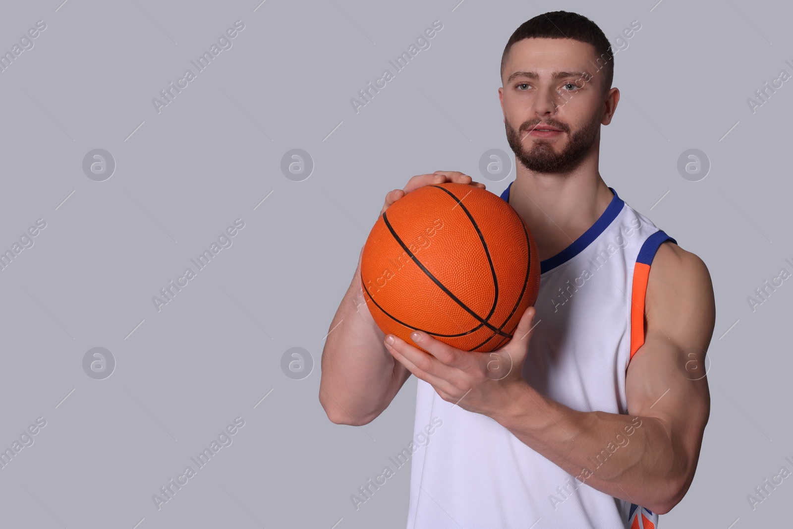 Photo of Athletic young man with basketball ball on light grey background. Space for text