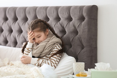 Photo of Sick little girl with tissue suffering from cold in bed