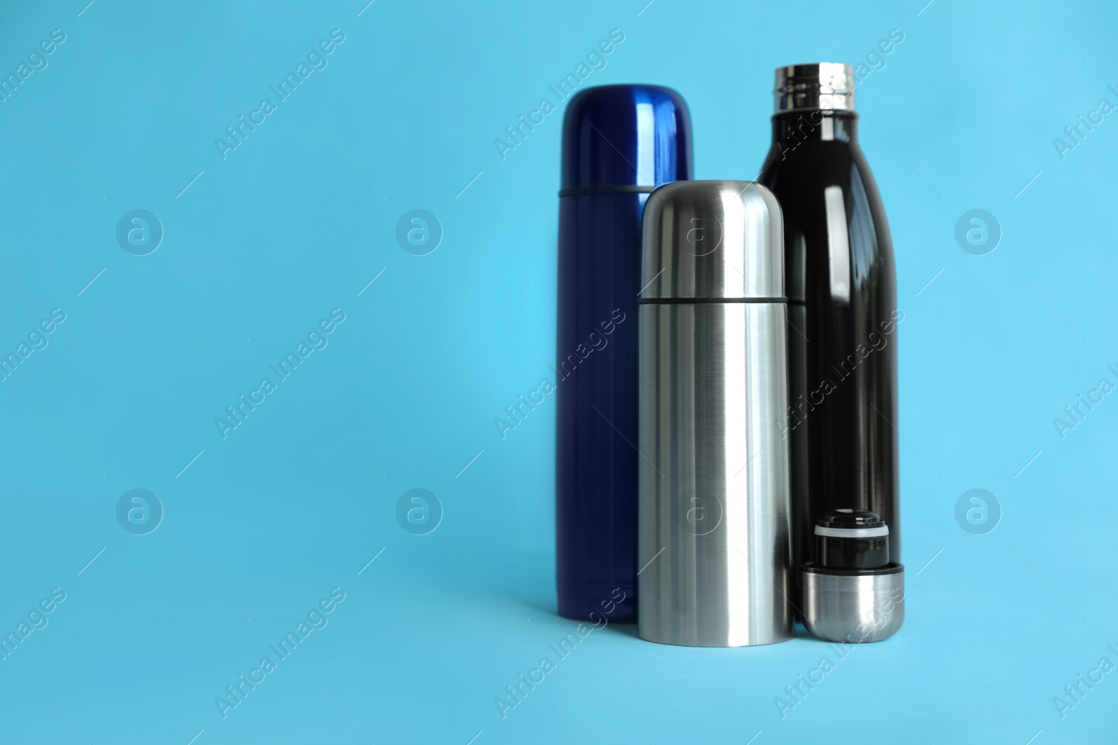 Photo of Stylish thermo bottles on light blue background, space for text