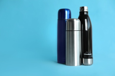 Stylish thermo bottles on light blue background, space for text