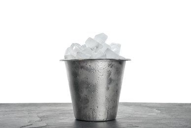 Metal bucket with ice cubes on table against white background