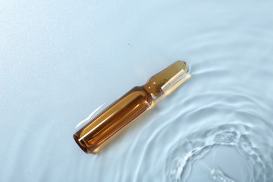 Skincare ampoule in water on light blue background, top view