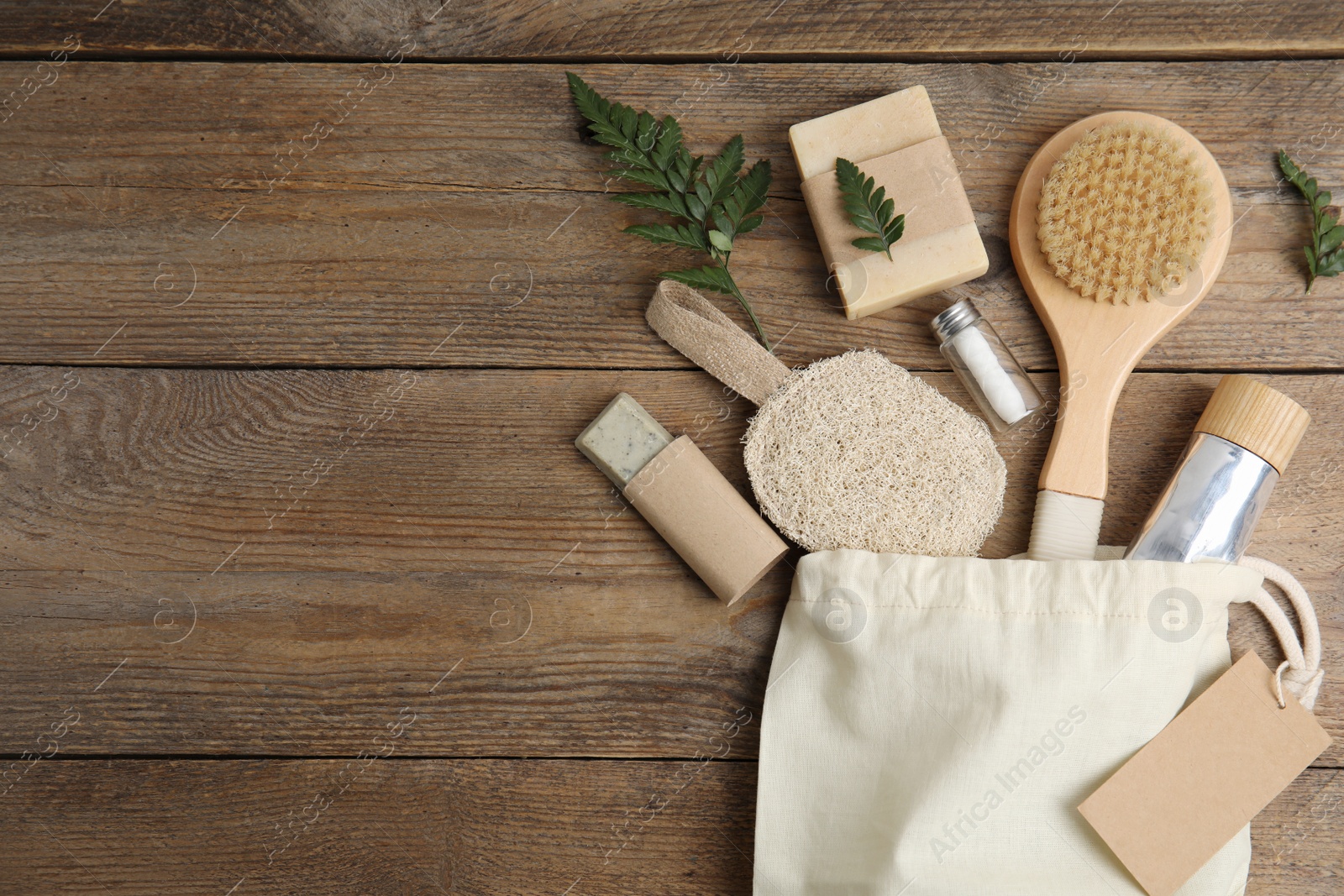 Photo of White cotton bag with eco friendly personal care products on wooden table, flat lay. Space for text