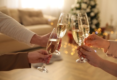 Photo of People clinking glasses of champagne in room decorated for Christmas, closeup. Holiday cheer and drink