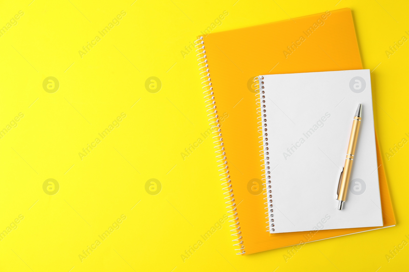 Photo of Notebooks and pen on yellow background, top view