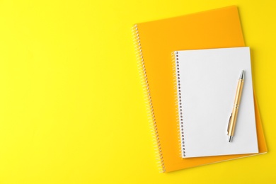 Photo of Notebooks and pen on yellow background, top view