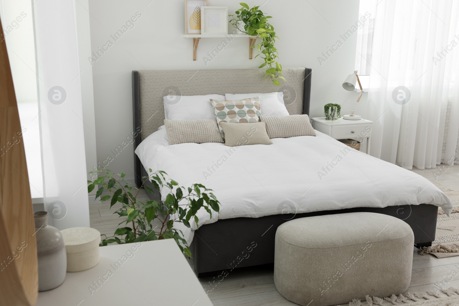 Photo of Stylish bedroom interior with large comfortable bed, ottoman and bedside table