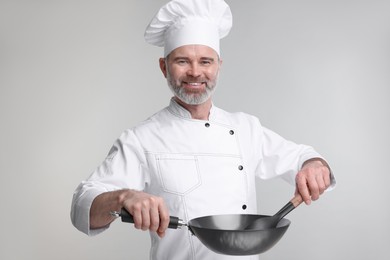 Happy chef in uniform with wok and spoon on grey background