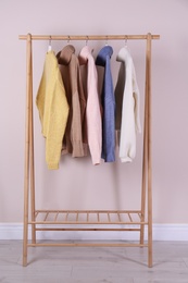 Warm sweaters hanging on wooden rack near pink wall
