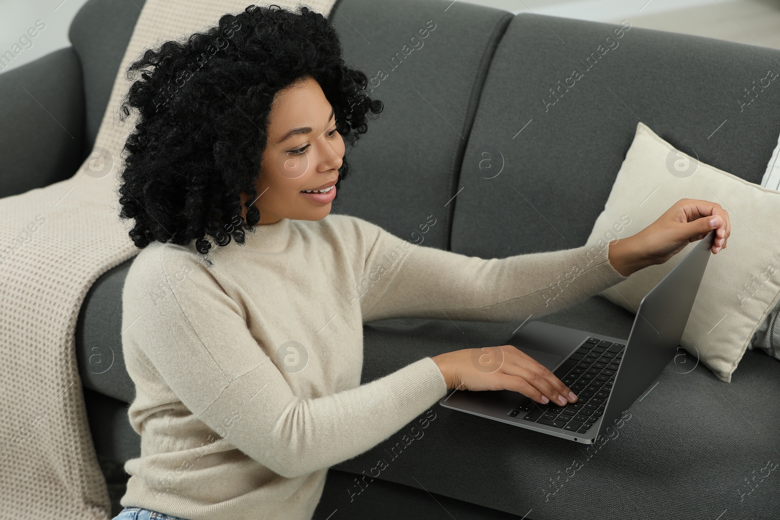 Photo of Happy young woman using laptop on sofa indoors