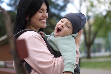 Mother holding her child in sling (baby carrier) on bench in park