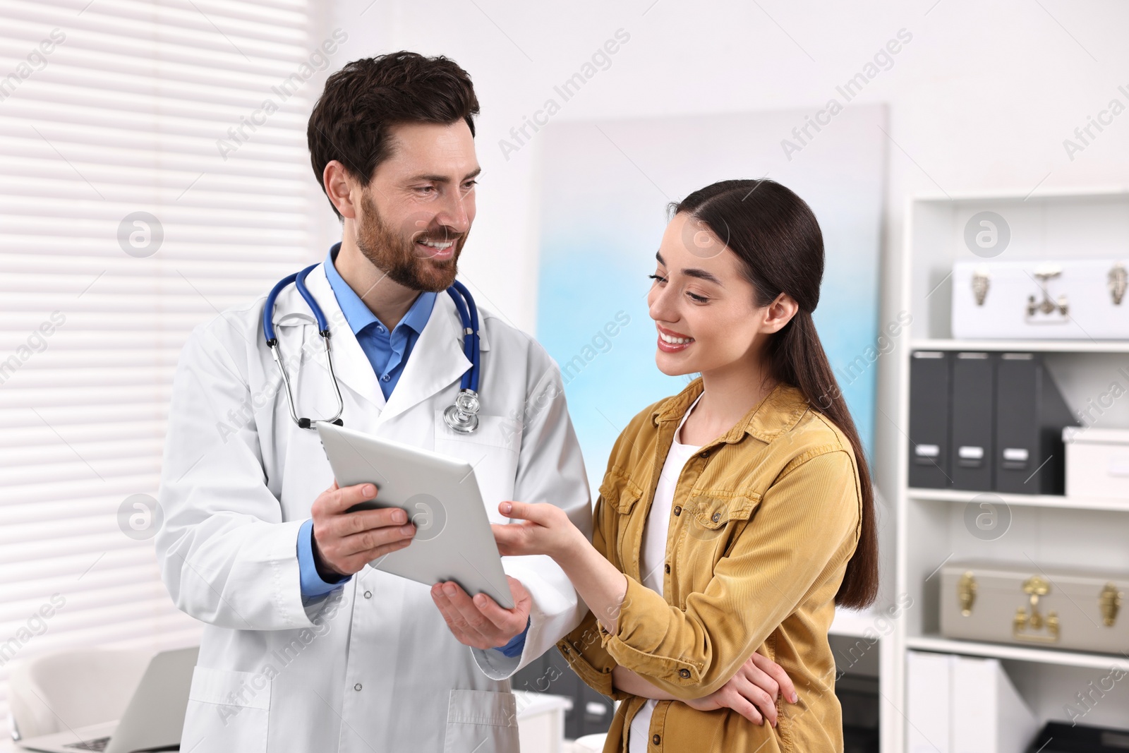 Photo of Doctor with tablet consulting patient during appointment in clinic