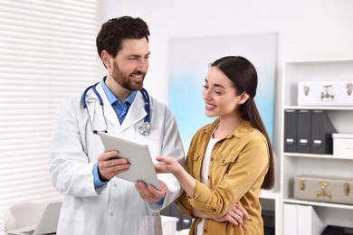 Photo of Doctor with tablet consulting patient during appointment in clinic