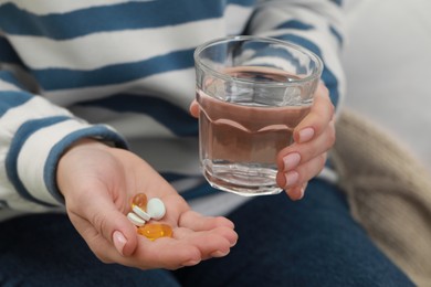 Woman with glass of water and pills indoors, closeup