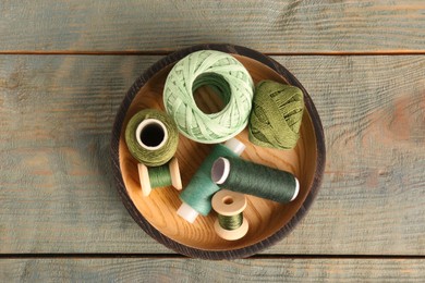 Photo of Color sewing threads in bowl on light blue wooden table, top view