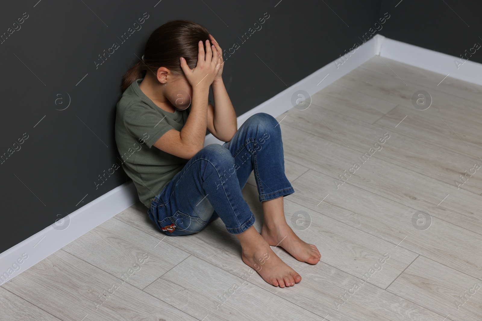 Photo of Child abuse. Upset girl sitting on floor near grey wall