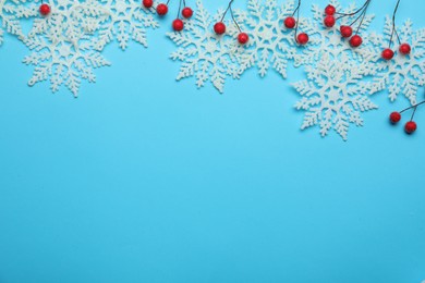 Photo of Beautiful decorative snowflakes and red berries on light blue background, flat lay. Space for text