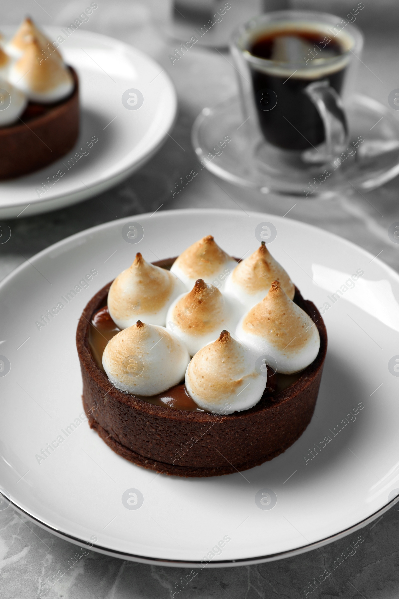 Photo of Delicious salted caramel chocolate tart with meringue served on light grey marble table, closeup