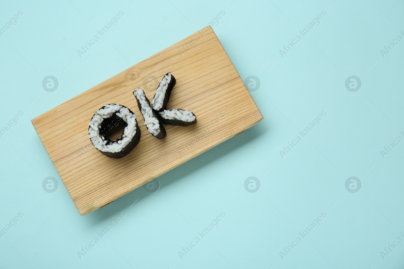 Photo of Serving board with word Ok made of sushi rolls on light turquoise background, top view. Space for text