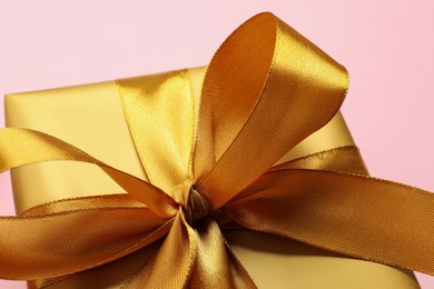 Beautiful golden gift box with bow on pink background, closeup