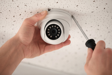 Photo of Technician installing CCTV camera on ceiling indoors, closeup